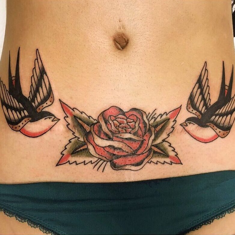 Tatuaż na brzuchu kobiety przedstawiający dwie jaskółki.
